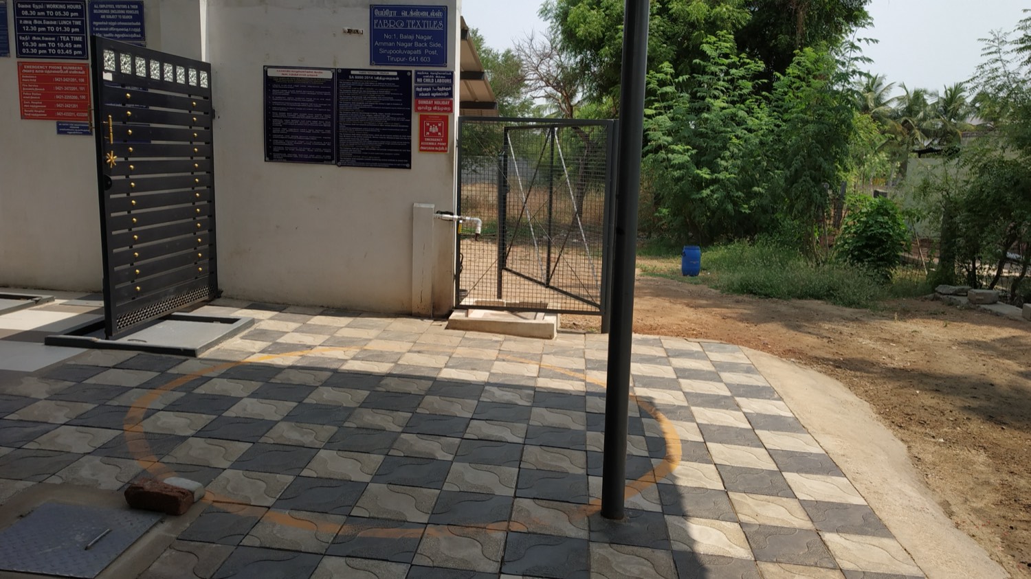 The entrance of the Fabro Textiles unit in Tirupur, with notice boards displaying the SA 8000 policy, working hours, emergency contact numbers, the no child labour notice and the emergency assembly point